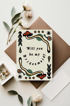 a card with the words will you be my bridesmaid on it next to some flowers