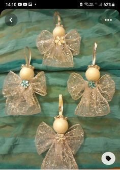 four glass angel ornaments with bows and pearls hanging from the sides on a green cloth