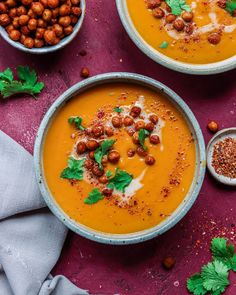 two bowls filled with carrot soup and garnished with parsley on the side