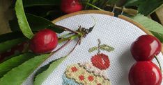 two cherries are on the table next to a cross - stitched cupcake