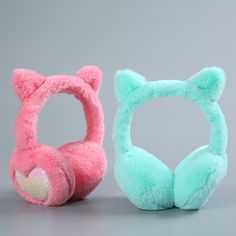 two stuffed animal headphones sitting next to each other on a gray surface, one pink and one blue