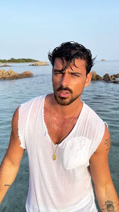 a man standing in the water wearing a white shirt and tattoos on his arm, looking at the camera