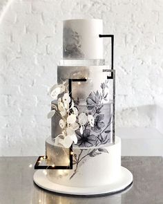 a three tiered cake with white flowers and black lines on the side, sitting on top of a table