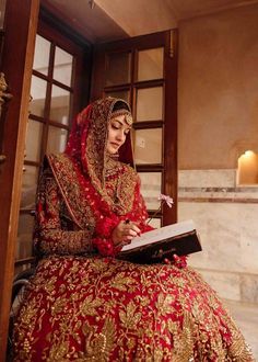 a woman in a red and gold bridal gown sitting on steps reading a book