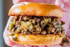 a close up of a person holding a sandwich with meat and vegetables on it in their hands