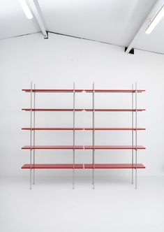 an empty white room with red shelves on the wall