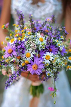 a bride holding a bouquet of wildflowers and daisies