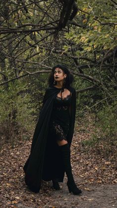 a woman dressed in black is standing on a path with trees and leaves around her