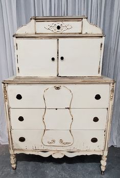 an old white dresser with black knobs on it's doors and drawer drawers