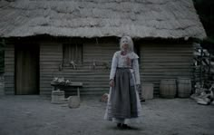 a woman standing in front of a house with a straw roof and thatched roof