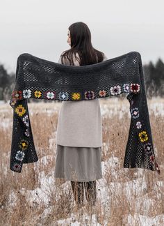 a woman standing in the snow holding up a black shawl with flowers on it