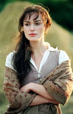 a woman with her arms crossed standing in front of hay bales and looking at the camera