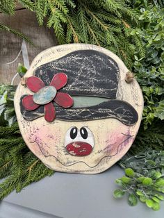 a wooden sign with a hat and flower on it sitting in front of some plants