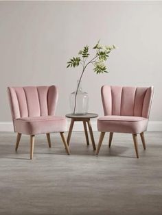 two pink chairs and a table with a vase on it