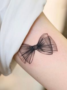 a woman's arm with a bow tattoo on the left side of her arm