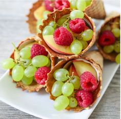 fruit and crackers are arranged on a white plate with raspberries, pears and grapes