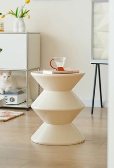 a white cat sitting on top of a wooden floor next to a vase with flowers