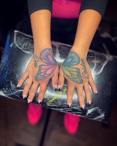 two hands with butterfly tattoos on them and one hand holding a piece of luggage in front of her