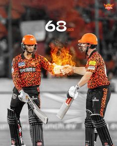 two men in orange and black uniforms holding baseball bats with flames coming out of them