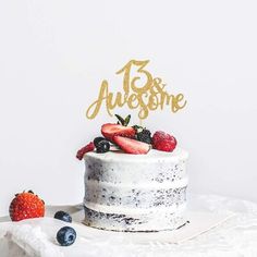 a white cake with berries and strawberries on top is sitting on a table in front of a white wall