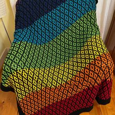 a multicolored knitted blanket sitting on top of a wooden floor next to a lamp