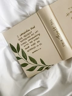 an open book laying on top of a white bed with writing on the front cover