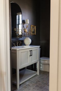 a white sink sitting under a bathroom mirror next to a toilet in a room with black walls