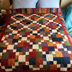 a bed with a colorful quilt on top of it next to two pillows and a night stand