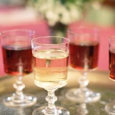 four glasses filled with liquid sitting on top of a metal tray next to each other