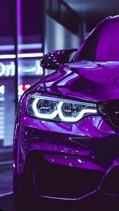 the front end of a purple bmw car parked in a parking lot at night with its lights on