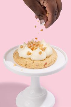 a person is sprinkling icing onto a cake on a white plate against a pink background