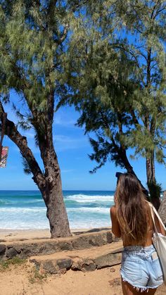 a woman standing on top of a sandy beach next to trees and the ocean in the background