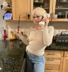 a woman standing in a kitchen holding a knife and looking at the camera with both hands