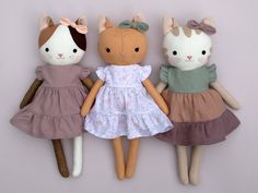 three stuffed animals are sitting next to each other on a white surface and one is wearing a pink dress