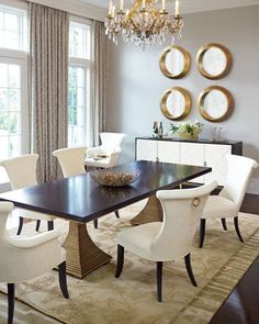 a dining room table with white chairs and a bowl on top of it in front of two mirrors