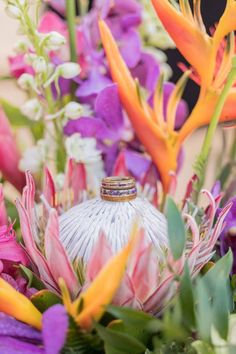 a wedding ring sits on top of a bouquet of purple and orange flowers in the foreground