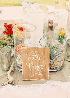 a wooden sign sitting on top of a table next to vases filled with flowers