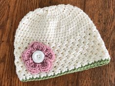 a crocheted hat with a button on the side sitting on a wooden surface