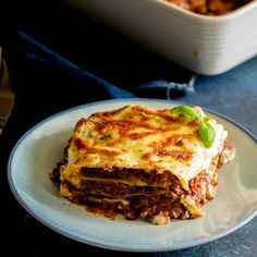 a white plate topped with lasagna next to a casserole dish