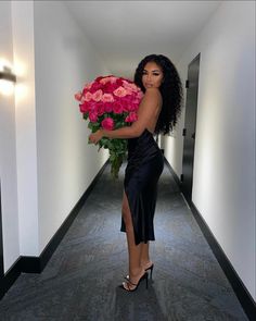 a woman in a long black dress holding a large bouquet of flowers on the hallway