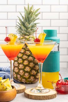 two cocktails with pineapple and cherries in front of a pineapple cooler