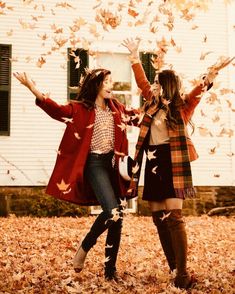 two girls are playing with leaves in front of a house