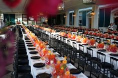 the long tables are set with black and white tablecloths, orange centerpieces, and clear glass vases