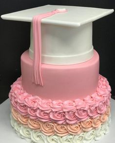 a pink and white graduation cake with roses on the bottom, topped with a cap