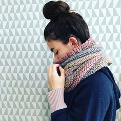 a woman wearing a knitted cowl neck scarf in front of a patterned wall