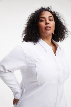 a woman with curly hair wearing a white shirt and gold hoop earrings, posing for the camera