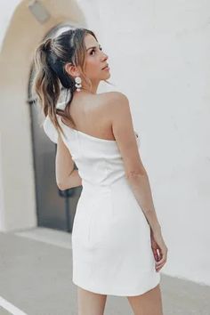 a woman in a white dress is walking down the street with her back to the camera