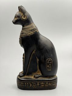 an egyptian cat statue sitting on top of a white surface with writing in gold and black