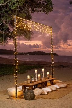 a wooden table with candles on it near the ocean at night under a lit up gazebo