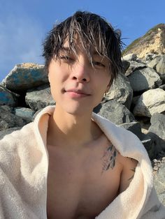 a shirtless young man standing in front of some rocks and looking at the camera